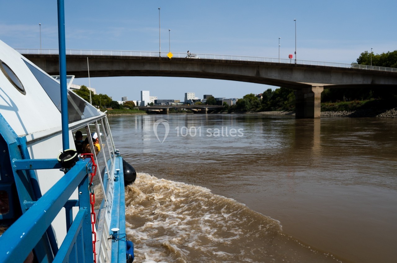 Vue depuis un bateau naviguant sur une rivière, avec un pont en béton et des bâtiments en arrière-plan.