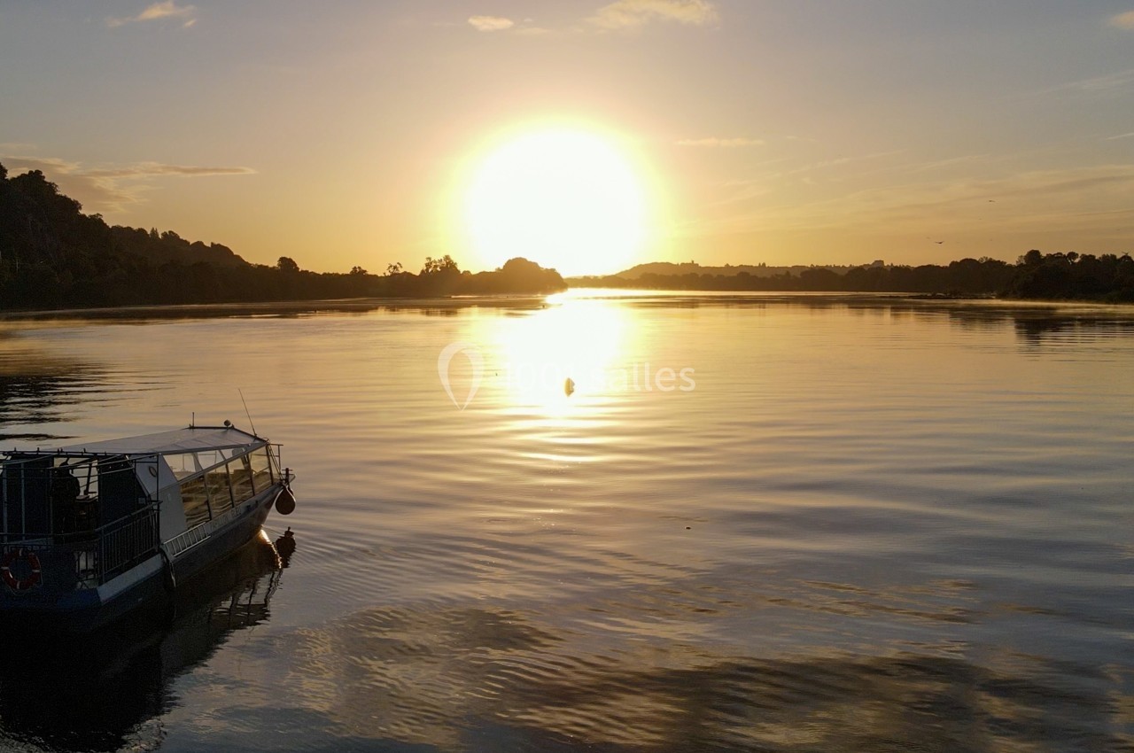 Bateau à l'arrêt sur une rivière calme au lever du soleil, entouré de collines et d'un ciel dégagé.