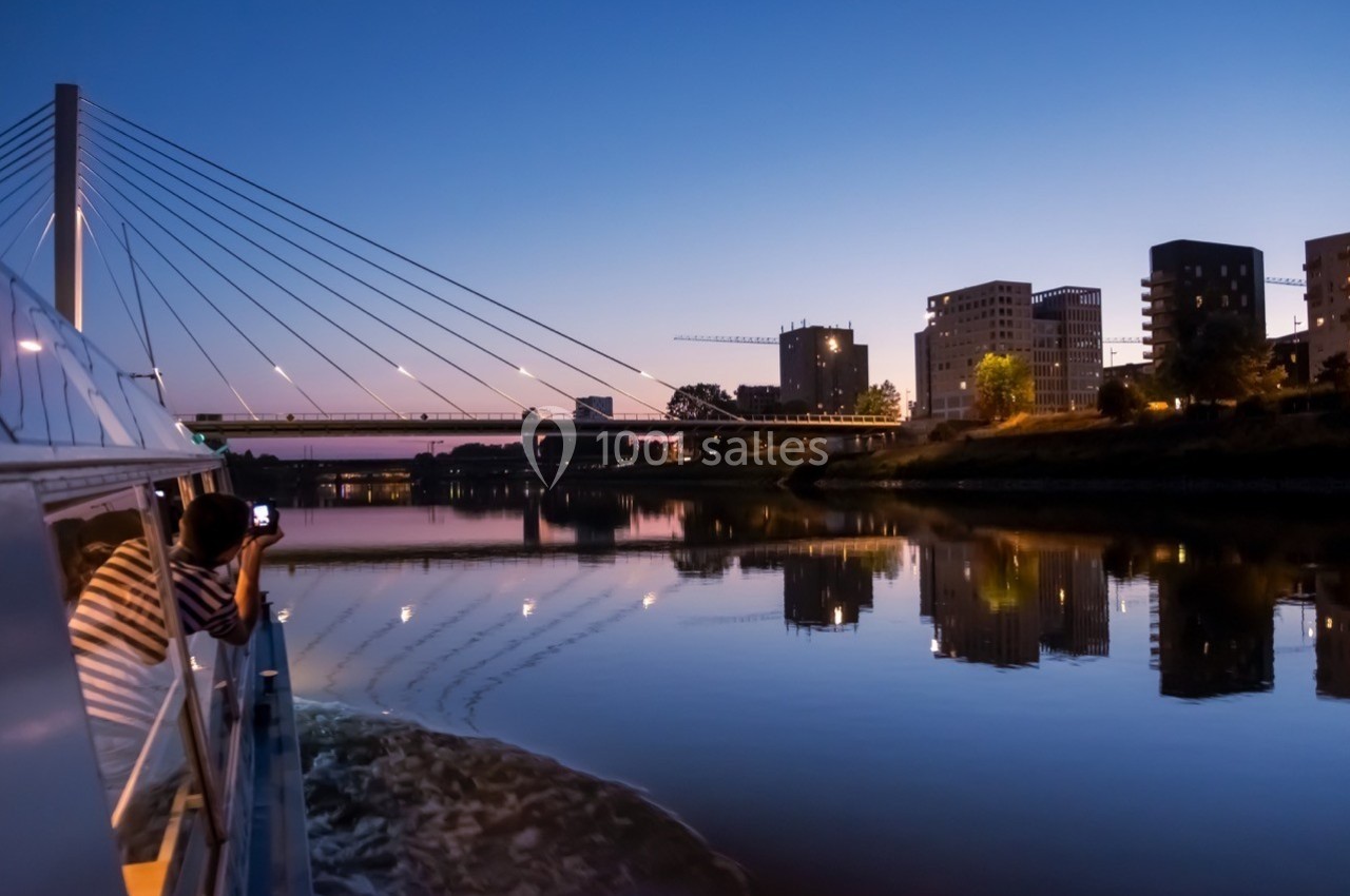 Vue d'un pont moderne et de bâtiments au bord d'une rivière au crépuscule, capturée depuis un bateau.