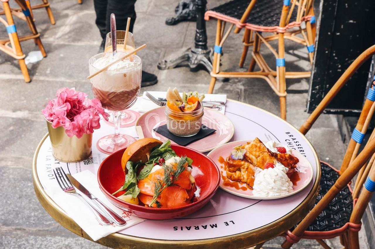 Assiette de saumon fumé, dessert, gaufres et boissons sur une table de café en terrasse avec chaises en arrière-plan.