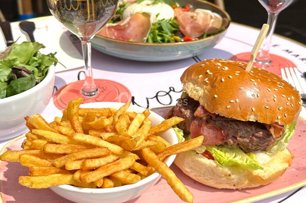 Assiette avec un burger garni de salade et tomate, accompagnée de frites, sur une table dressée en extérieur.