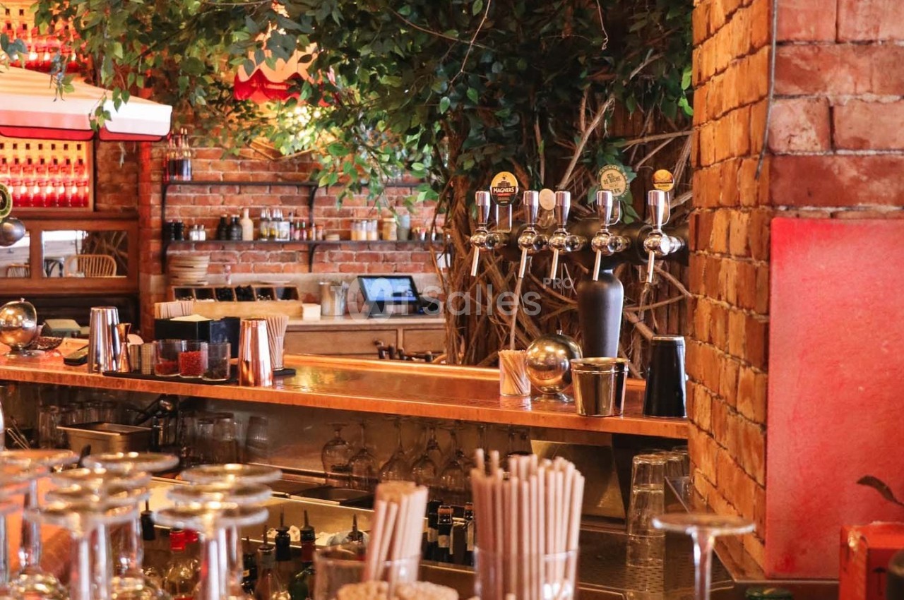 Comptoir de bar en bois avec tireuses à bière, verres et décorations végétales dans un intérieur en briques rouges.