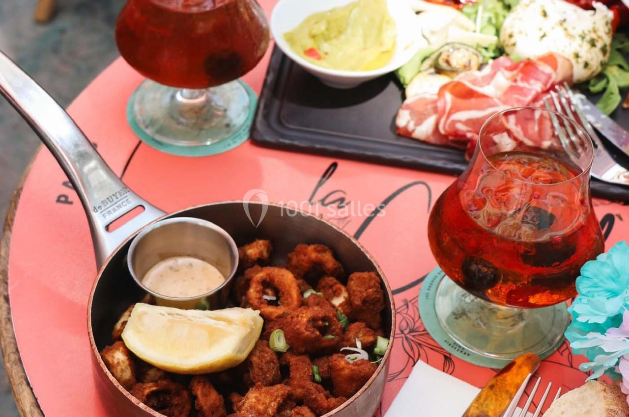 Assiette de calamars frits avec une tranche de citron et une sauce, accompagnée de verres de boisson et d'autres plats.