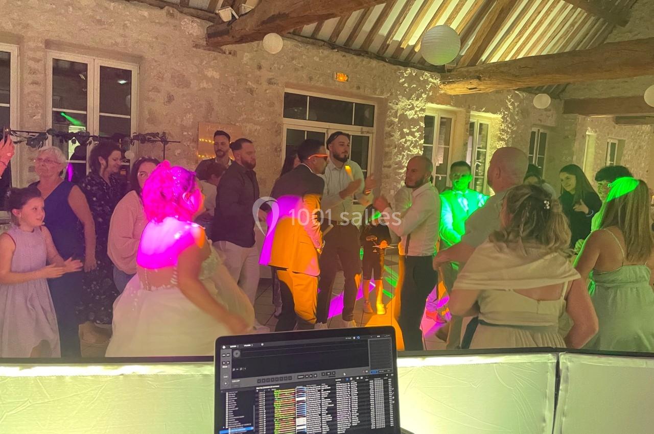 Des invités dansent et discutent dans une salle en pierre éclairée par des lumières colorées, vue depuis une table de DJ.
