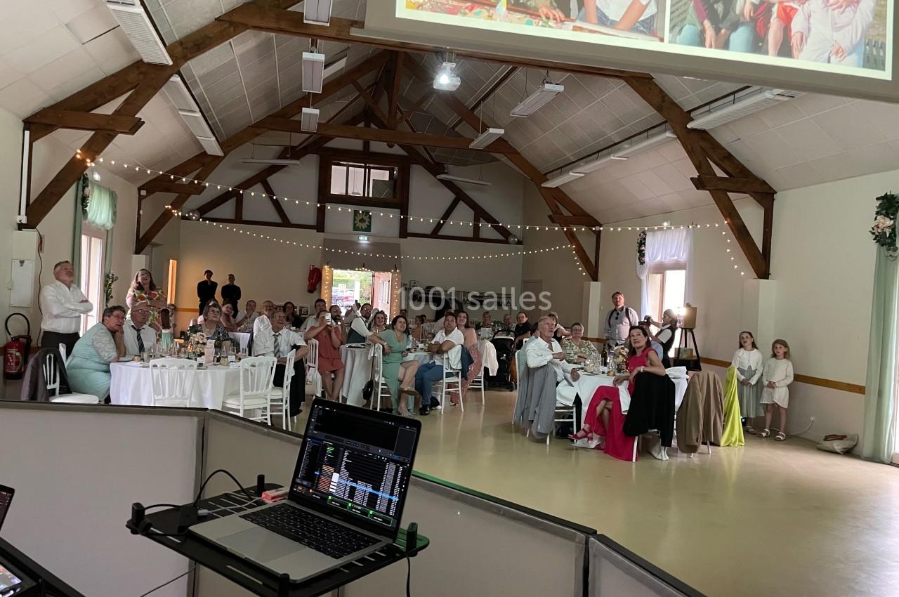 Invités assis dans une salle de réception décorée, regardant une projection lors d'un événement festif.