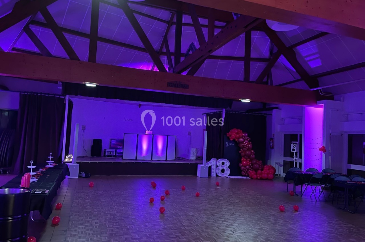 Salle décorée pour une fête, éclairée de lumières violettes, avec des ballons rouges et un chiffre ’18’ en ballons.