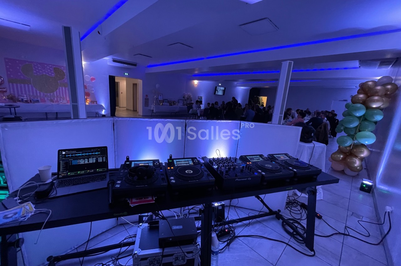 Poste de DJ avec platines, ordinateur et éclairage, dans une salle de réception décorée de ballons et éclairée en bleu.