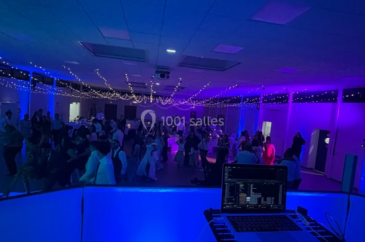 Salle de réception éclairée de lumières colorées, avec des invités dansant et un poste de DJ au premier plan.