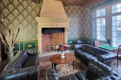 Salon ancien avec parquet en bois, mobilier classique, cheminée, miroir, coiffeuse et grande fenêtre avec rideaux roses.