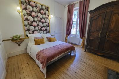 Salon ancien avec parquet en bois, mobilier classique, cheminée, miroir, coiffeuse et grande fenêtre avec rideaux roses.