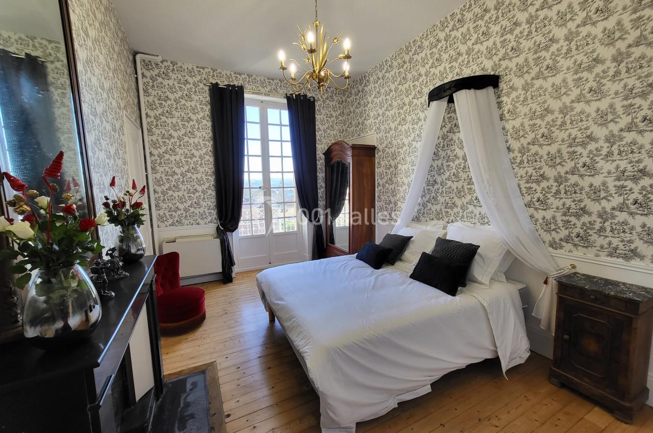 Chambre lumineuse avec lit double à baldaquin, parquet en bois, cheminée, armoire et fenêtre donnant sur l'extérieur.