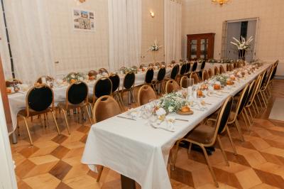 Salon ancien avec parquet en bois, mobilier classique, cheminée, miroir, coiffeuse et grande fenêtre avec rideaux roses.