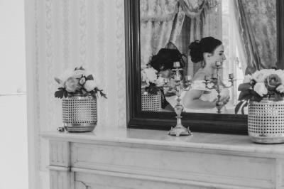 Salon ancien avec parquet en bois, mobilier classique, cheminée, miroir, coiffeuse et grande fenêtre avec rideaux roses.