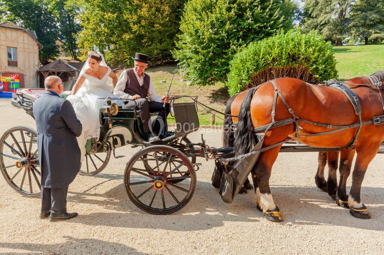 Une mariée monte dans une calèche tirée par deux chevaux, accompagnée d'un cocher et d'un homme en costume.