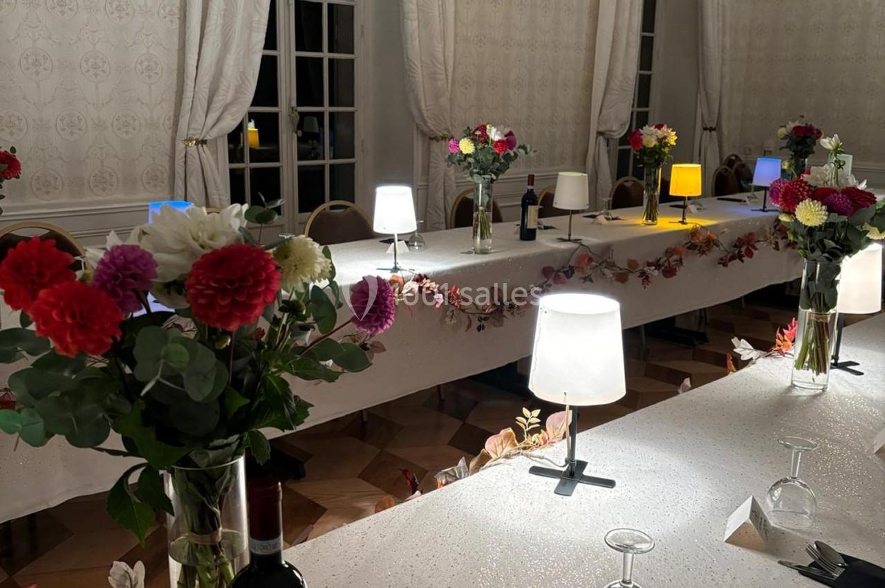 Salle de réception décorée avec des fleurs colorées, des guirlandes et des lampes sur des tables blanches.