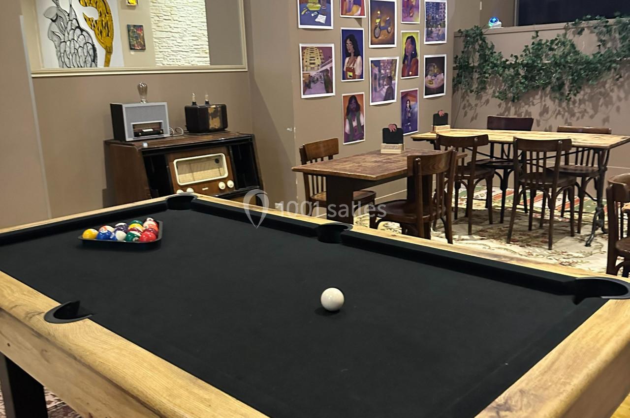 Table de billard noir dans une salle décorée avec des affiches colorées, des tables en bois et une ambiance rétro.