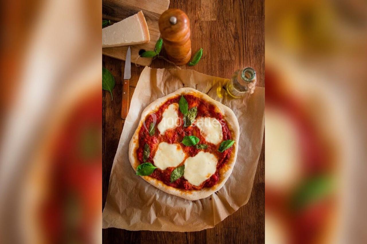 Pizza margherita sur papier cuisson, garnie de mozzarella fondue, sauce tomate et feuilles de basilic, sur une table en bois.