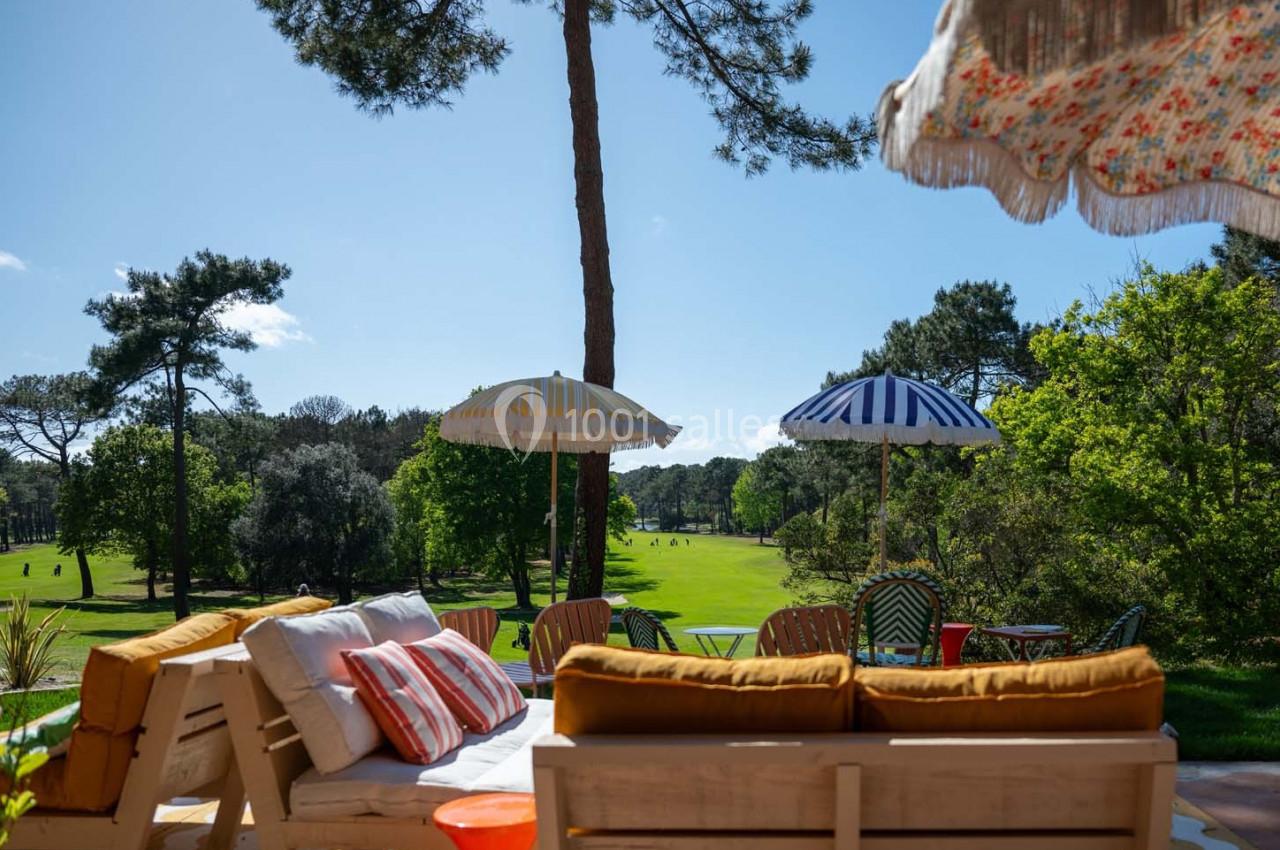 Terrasse aménagée avec canapés et parasols colorés, donnant sur un terrain de golf entouré de verdure.