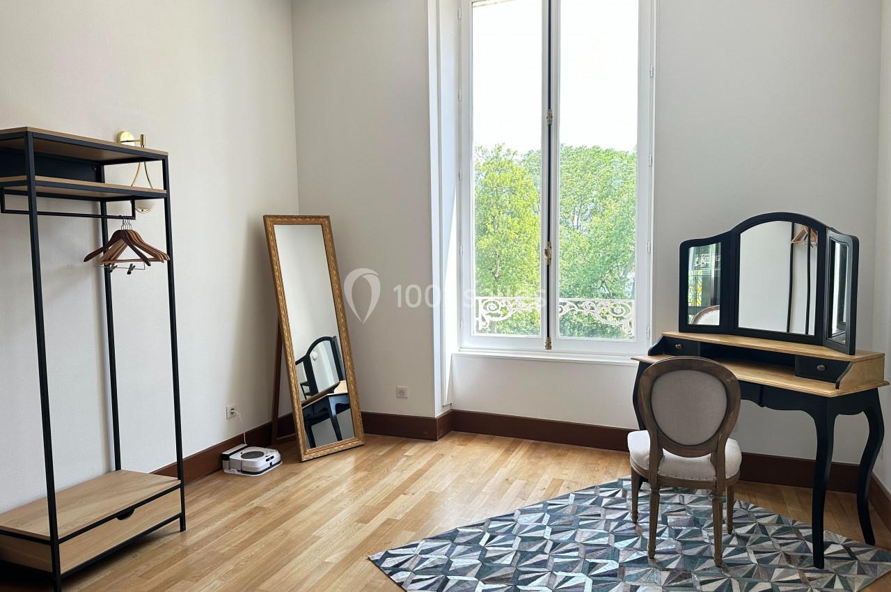 Chambre lumineuse avec coiffeuse, miroir sur pied, portant en métal et parquet en bois clair.