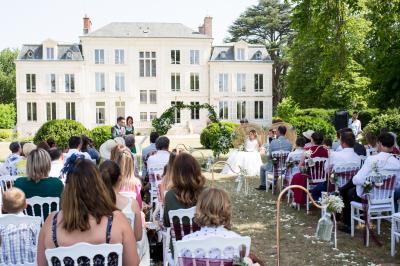 Un groupe de musiciens joue en plein air devant un grand bâtiment de style classique, entouré d'invités en tenue claire.