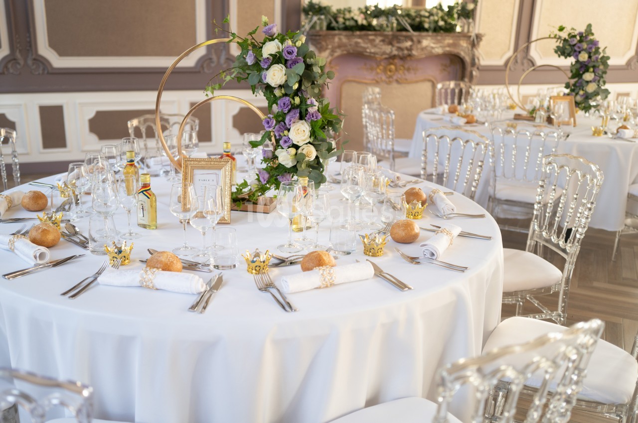 Table de réception élégamment dressée avec nappes blanches, chaises transparentes, fleurs et décorations raffinées.