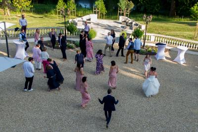 Un groupe de musiciens joue en plein air devant un grand bâtiment de style classique, entouré d'invités en tenue claire.