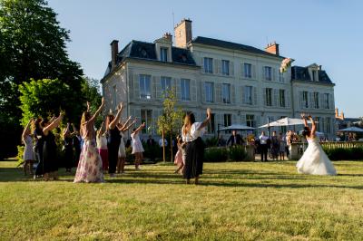 Un groupe de musiciens joue en plein air devant un grand bâtiment de style classique, entouré d'invités en tenue claire.