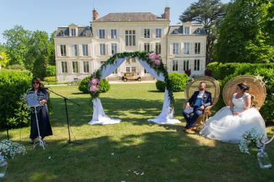 Un groupe de musiciens joue en plein air devant un grand bâtiment de style classique, entouré d'invités en tenue claire.