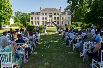 Un groupe de musiciens joue en plein air devant un grand bâtiment de style classique, entouré d'invités en tenue claire.