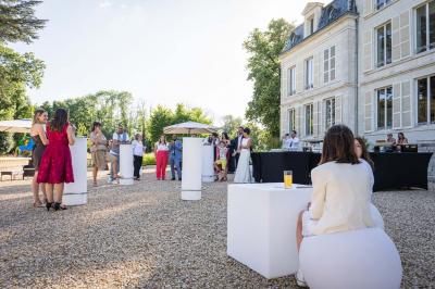 Un groupe de musiciens joue en plein air devant un grand bâtiment de style classique, entouré d'invités en tenue claire.