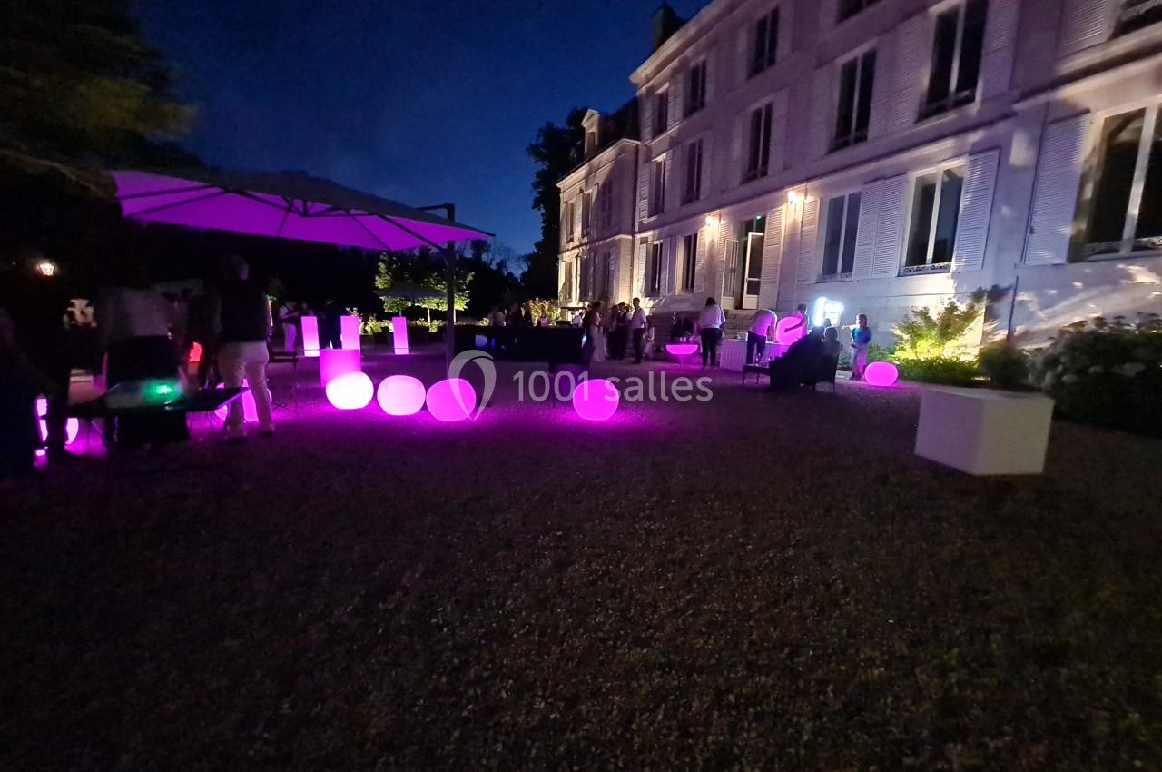 Cour d'un bâtiment éclairé la nuit, avec des sphères lumineuses violettes et des invités rassemblés.