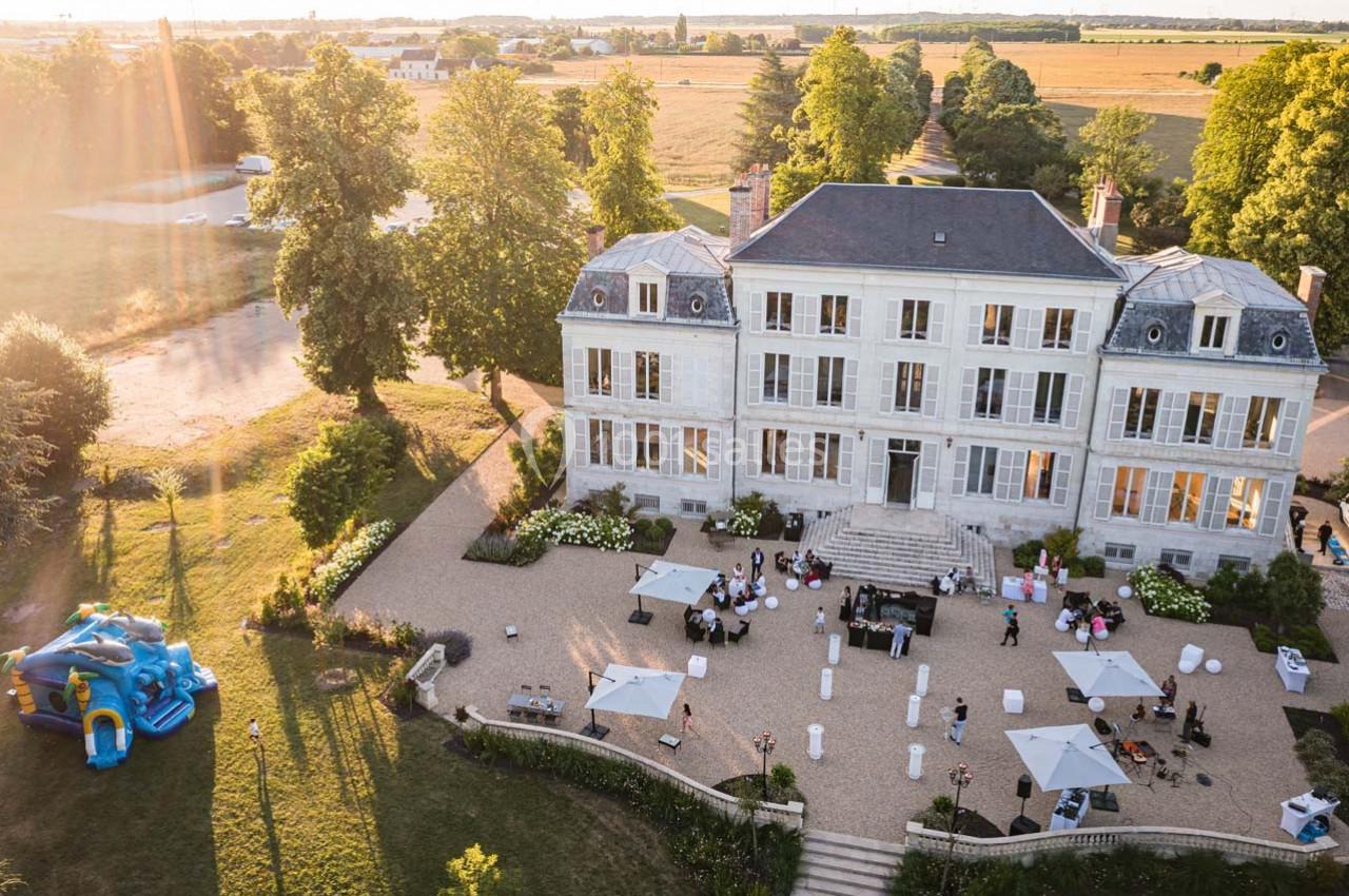 Vue aérienne d'un manoir entouré de jardins, avec une réception en plein air et une structure gonflable pour enfants.