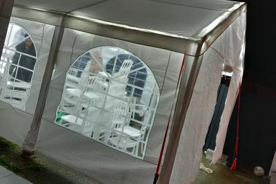 Intérieur d'une tente blanche avec des parois transparentes laissant voir un jardin et une porte en bois.