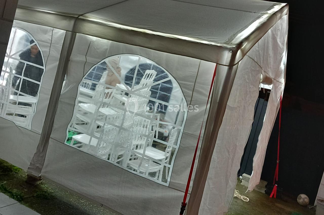 Tente blanche éclairée avec des chaises empilées visibles à travers les fenêtres en plastique transparent.