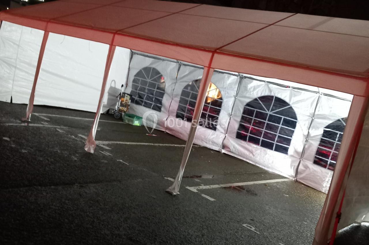 Tente blanche installée sur un parking, éclairée de l'intérieur avec des fenêtres en plastique transparent.