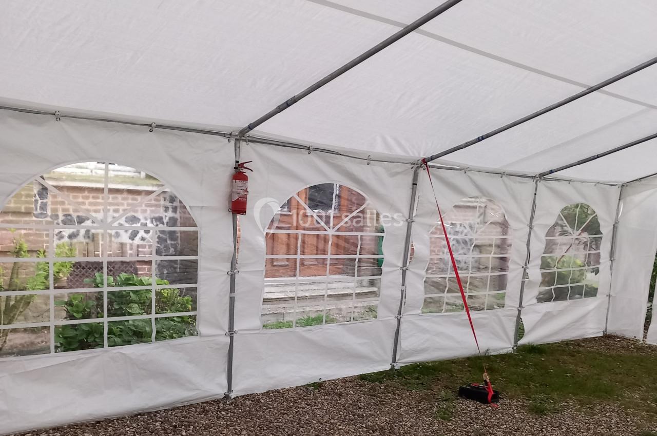 Intérieur d'une tente blanche avec des fenêtres en plastique transparent donnant sur un mur en pierre et des portes en bois.