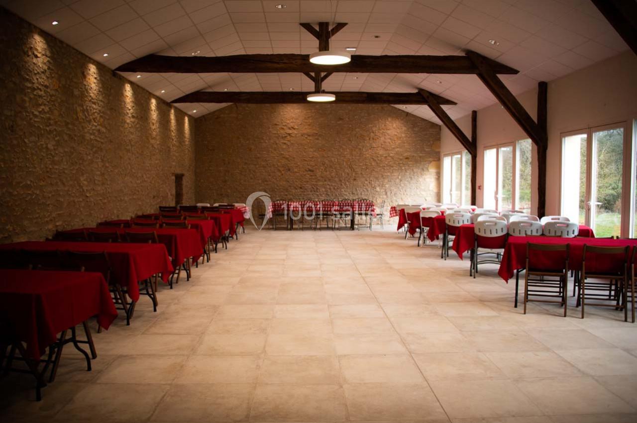 Salle spacieuse avec murs en pierre, tables dressées avec nappes rouges et grandes fenêtres laissant entrer la lumière.