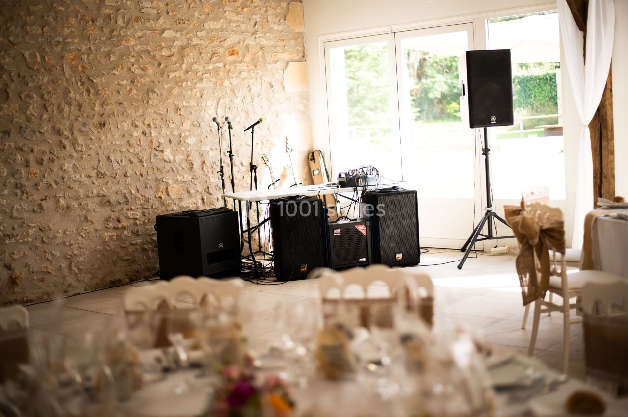 Équipement de sonorisation installé dans une salle lumineuse avec murs en pierre et tables décorées pour un événement.