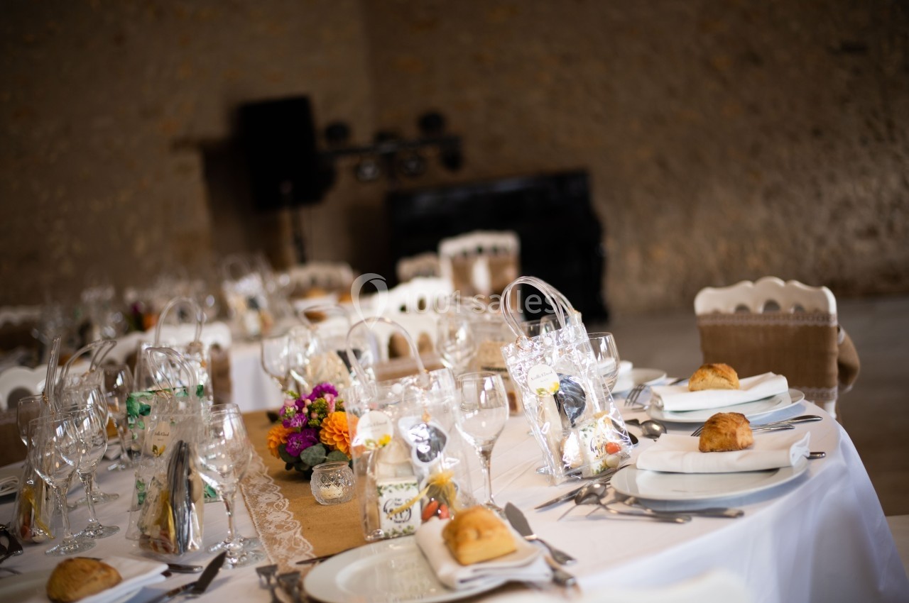 Table de réception élégamment dressée avec nappes blanches, verres, couverts, fleurs et petits cadeaux pour les invités.