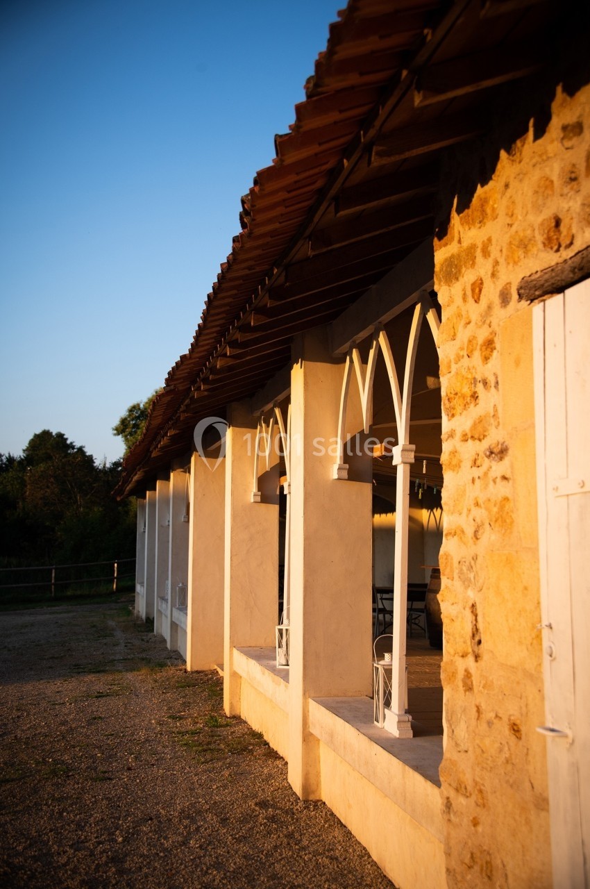 Façade d'un bâtiment en pierre avec des arches blanches, éclairée par une lumière chaude au coucher du soleil.