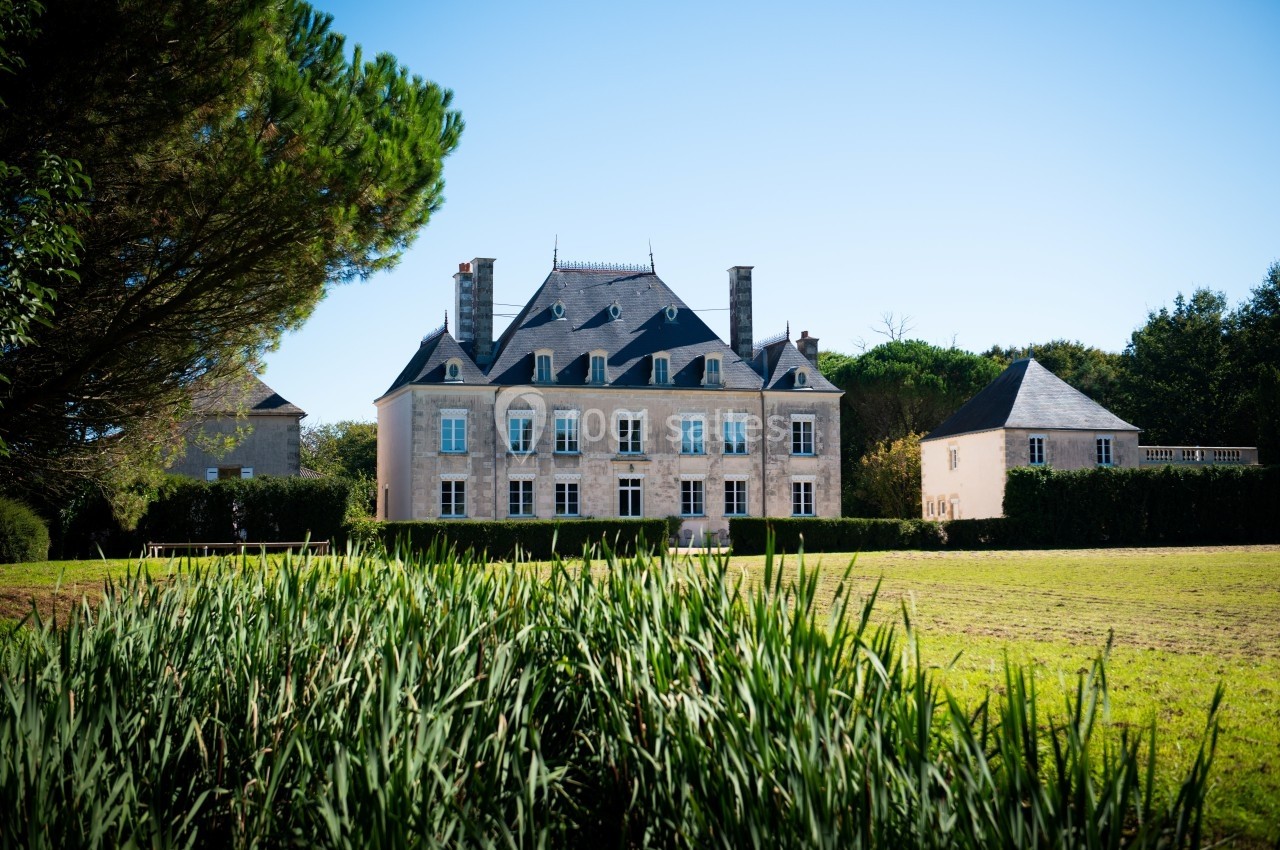 Manoir en pierre entouré de verdure, avec pelouse au premier plan et ciel dégagé en arrière-plan.