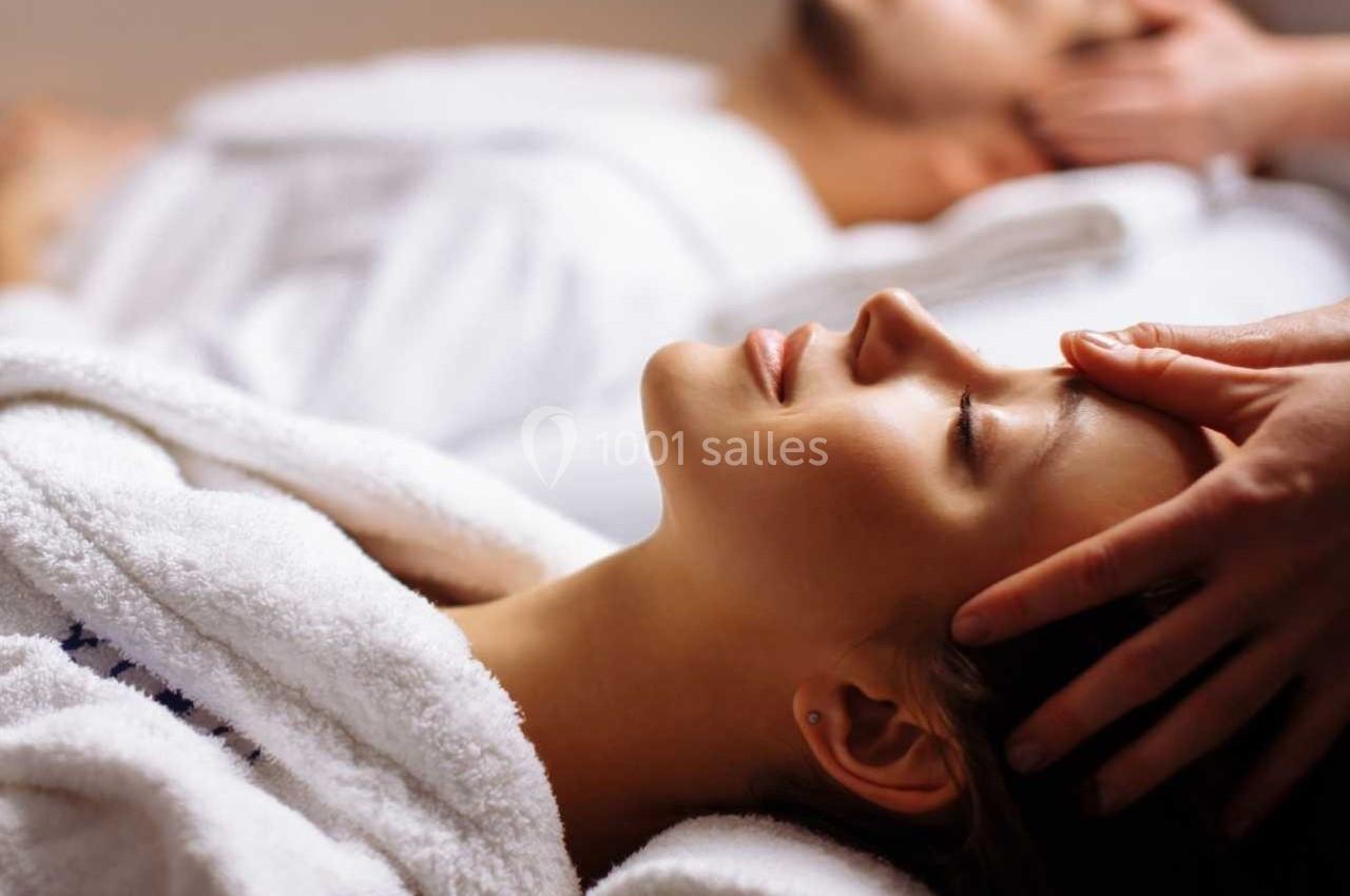 BIEN ETRE Deux personnes en peignoir blanc reçoivent un massage relaxant de la tête dans un cadre apaisant.