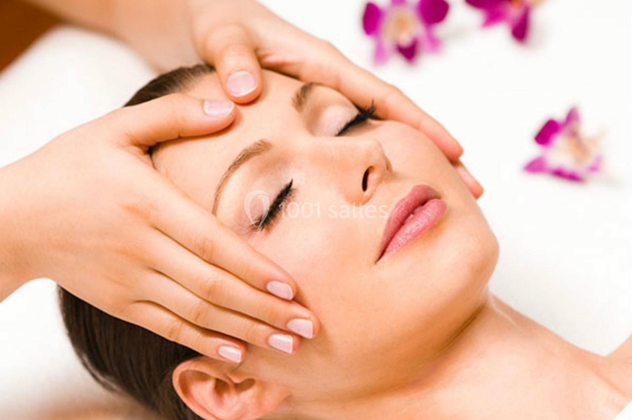BIEN ETRE Femme recevant un massage du visage, allongée sur une table, entourée de fleurs violettes.