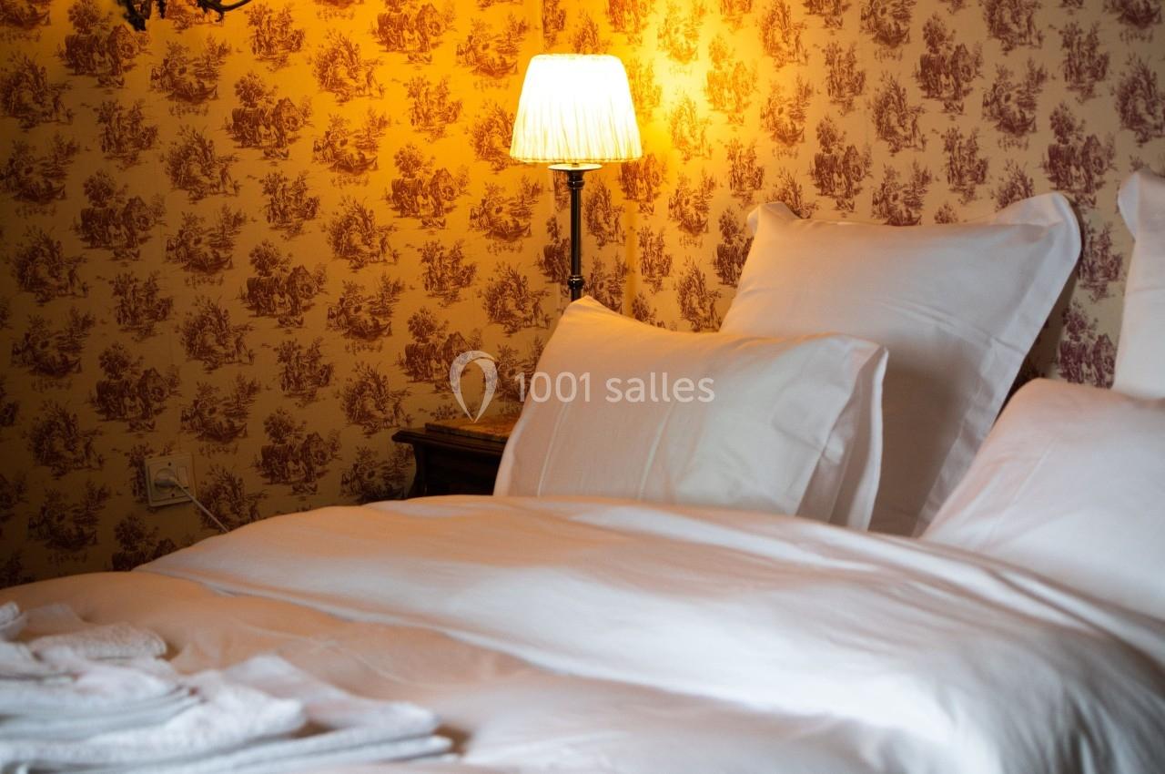 CHAMBRE D'HOTES Lit avec draps blancs impeccables, éclairé par une lampe de chevet et une applique murale, dans une chambre au papier peint…