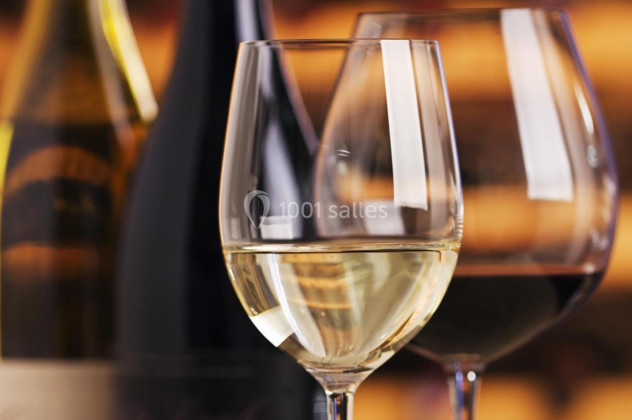 REPAS Deux verres de vin, l'un blanc et l'autre rouge, posés devant des bouteilles floues en arrière-plan.