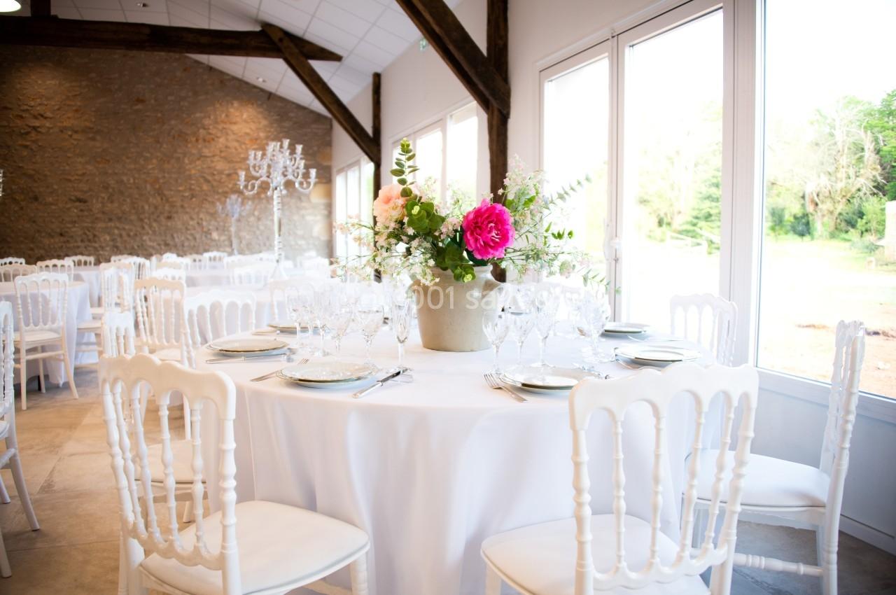 SALLE RIGOLETTO Salle de réception lumineuse avec tables rondes dressées, décorées de fleurs dans un vase central.