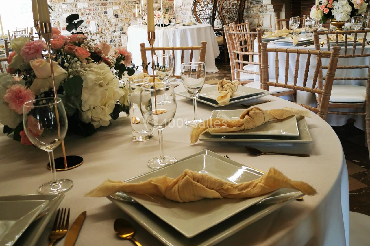 Location salle Saint-Samson-de-la-Roque (Eure) - Manoir Néo Normand #6 Table dressée avec élégance dans une salle en pierre, ornée de fleurs, bougies et vaisselle raffinée.