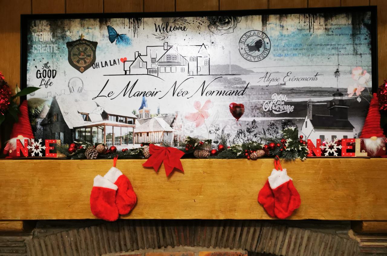 Location salle Saint-Samson-de-la-Roque (Eure) - Manoir Néo Normand #57 Décoration de Noël avec guirlandes, chaussettes rouges et panneau illustré du Manoir Néo Normand sur une cheminée en bois.