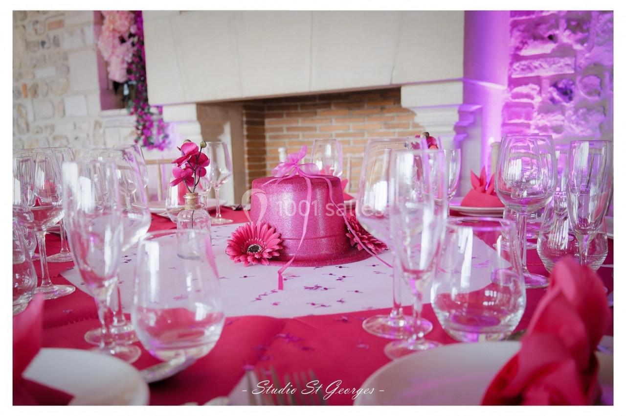 Location salle Saint-Samson-de-la-Roque (Eure) - Manoir Néo Normand #76 Table décorée pour une réception avec nappe rose, verres, fleurs et un gâteau rose au centre devant une cheminée.