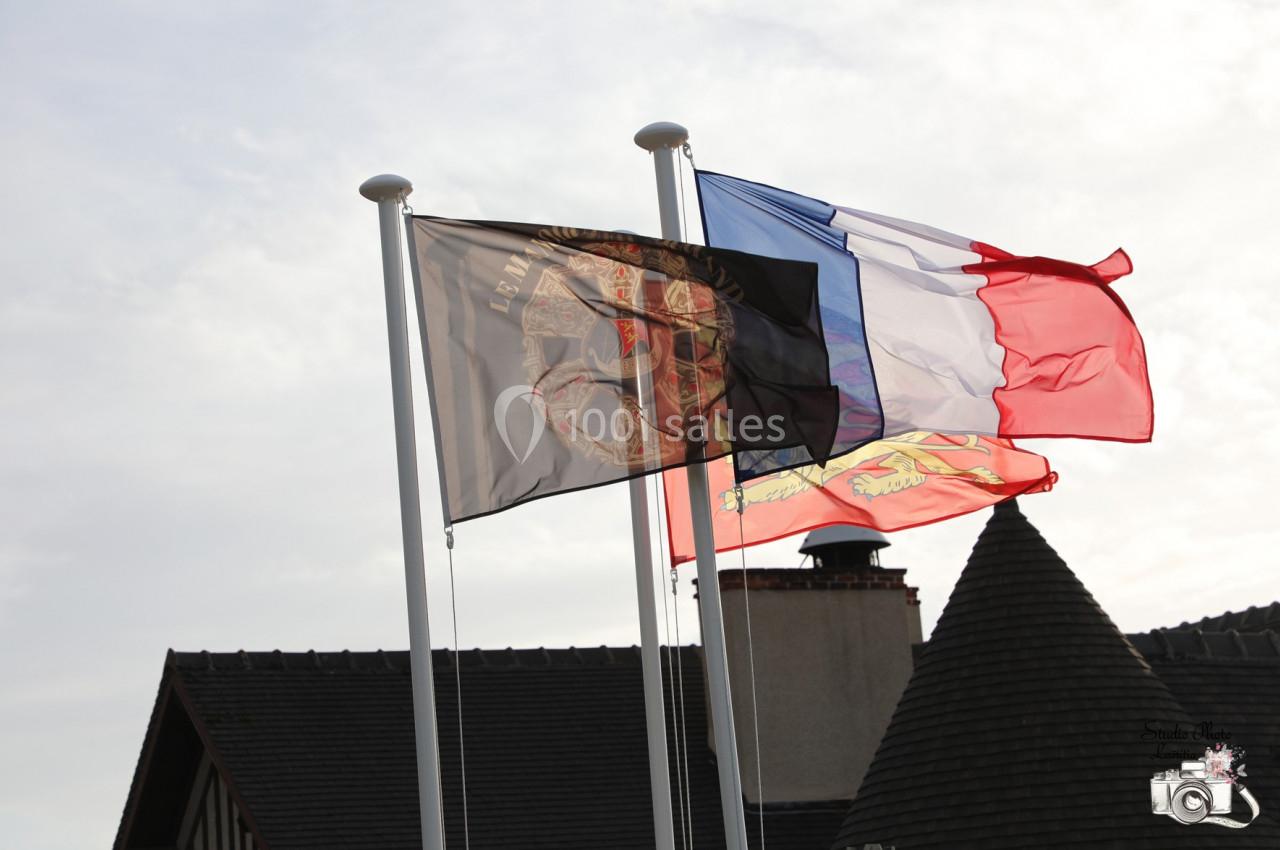 Location salle Saint-Samson-de-la-Roque (Eure) - Manoir Néo Normand #86 Trois drapeaux flottant au vent, dont le drapeau français, devant des toits en ardoise et une cheminée.